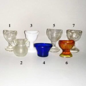 Collection of seven antique glass eye wash cups including clear, cobalt blue, amber, and milk glass examples with pedestal and squat forms, dating from the late 1800s to early 1900s