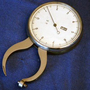 Antique mid-20th century lens thickness gauge with large calibrated dial face and curved brass caliper arms, used by opticians to measure ophthalmic spectacle lens thickness